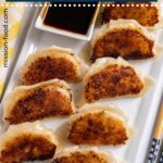 Pan-fried pork and shrimp dumplings arranged crispy side up on a white rectangular plate.