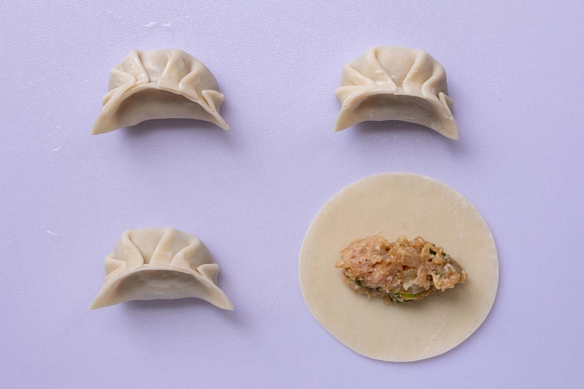 Pinching dumplings closed with pleated edges on a white cutting board.