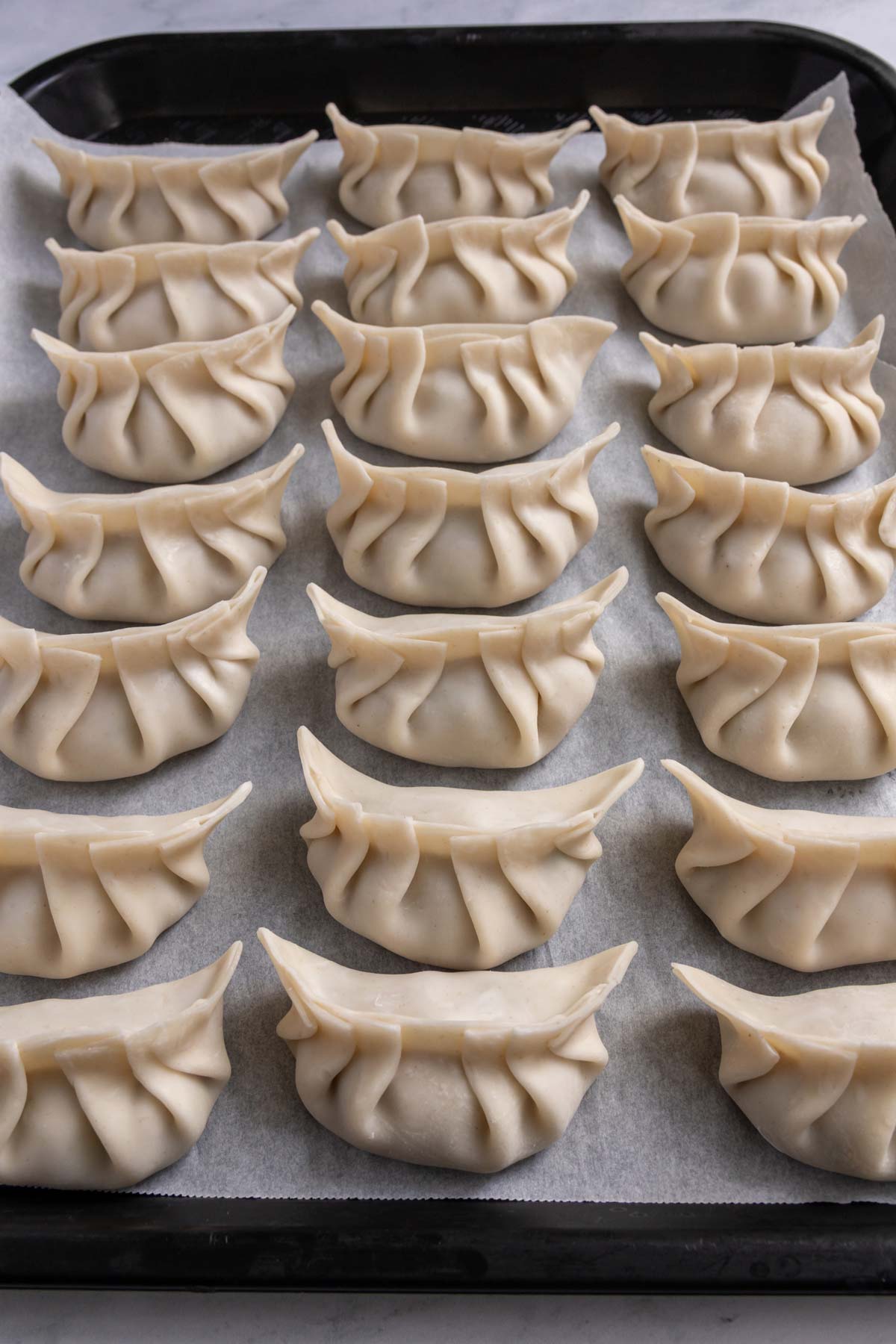 Three rows of assembled dumplings on a parchment lined tray.