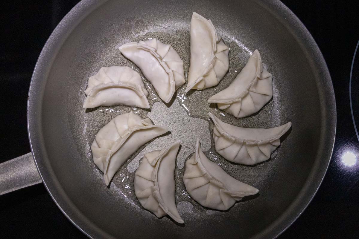 Uncooked dumplings arranged in a spiral pattern in a nonstick frying pan.