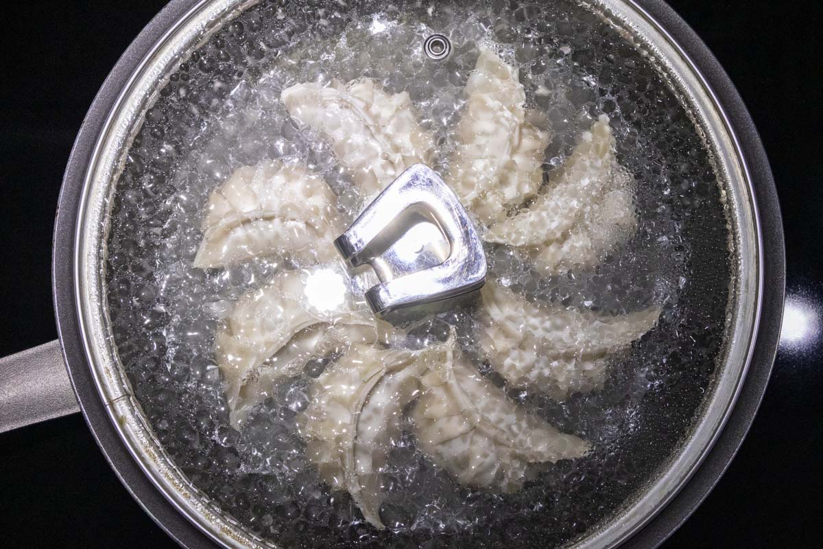 A glass lid covering a pan of dumplings that are cooking.