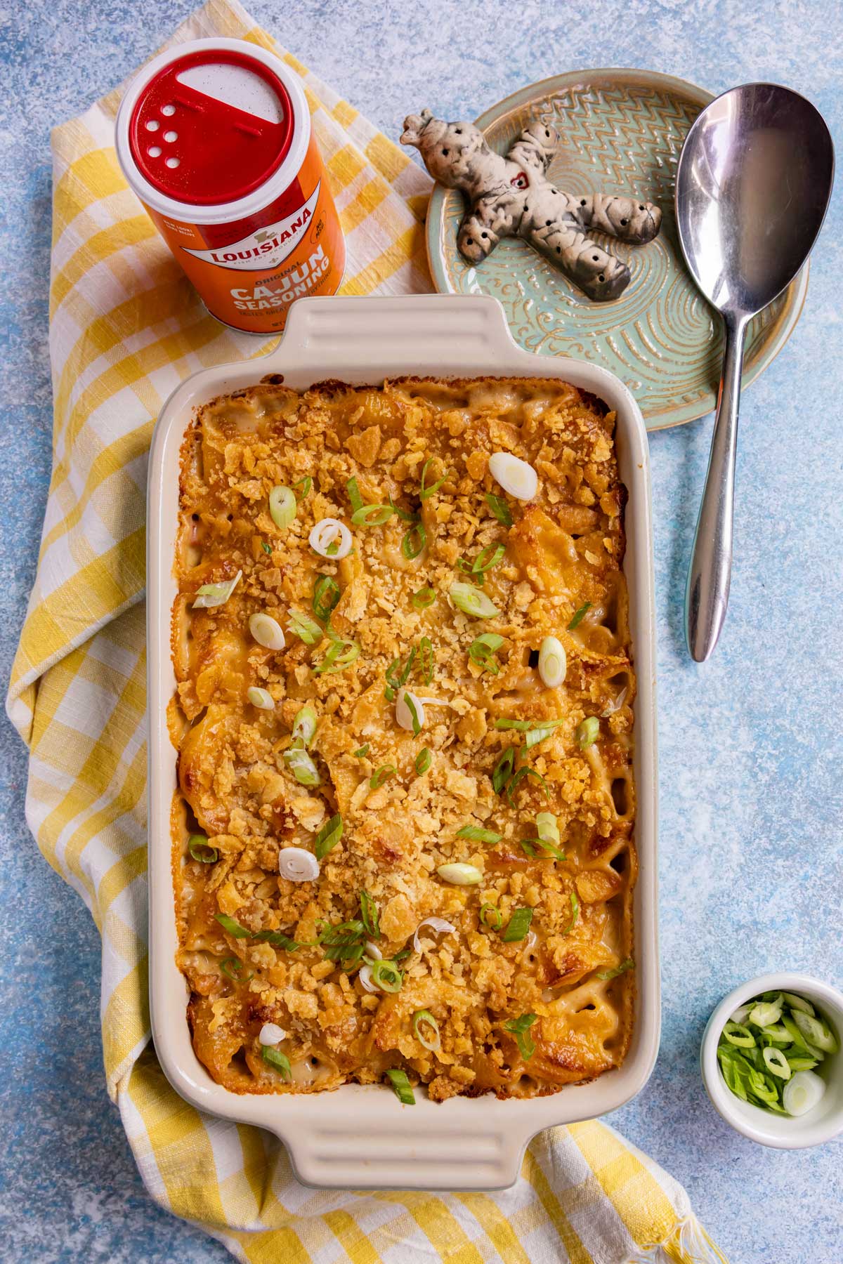 A Cajun mac and cheese casserole, a container of Cajun seasoning, and a voodoo doll plate.