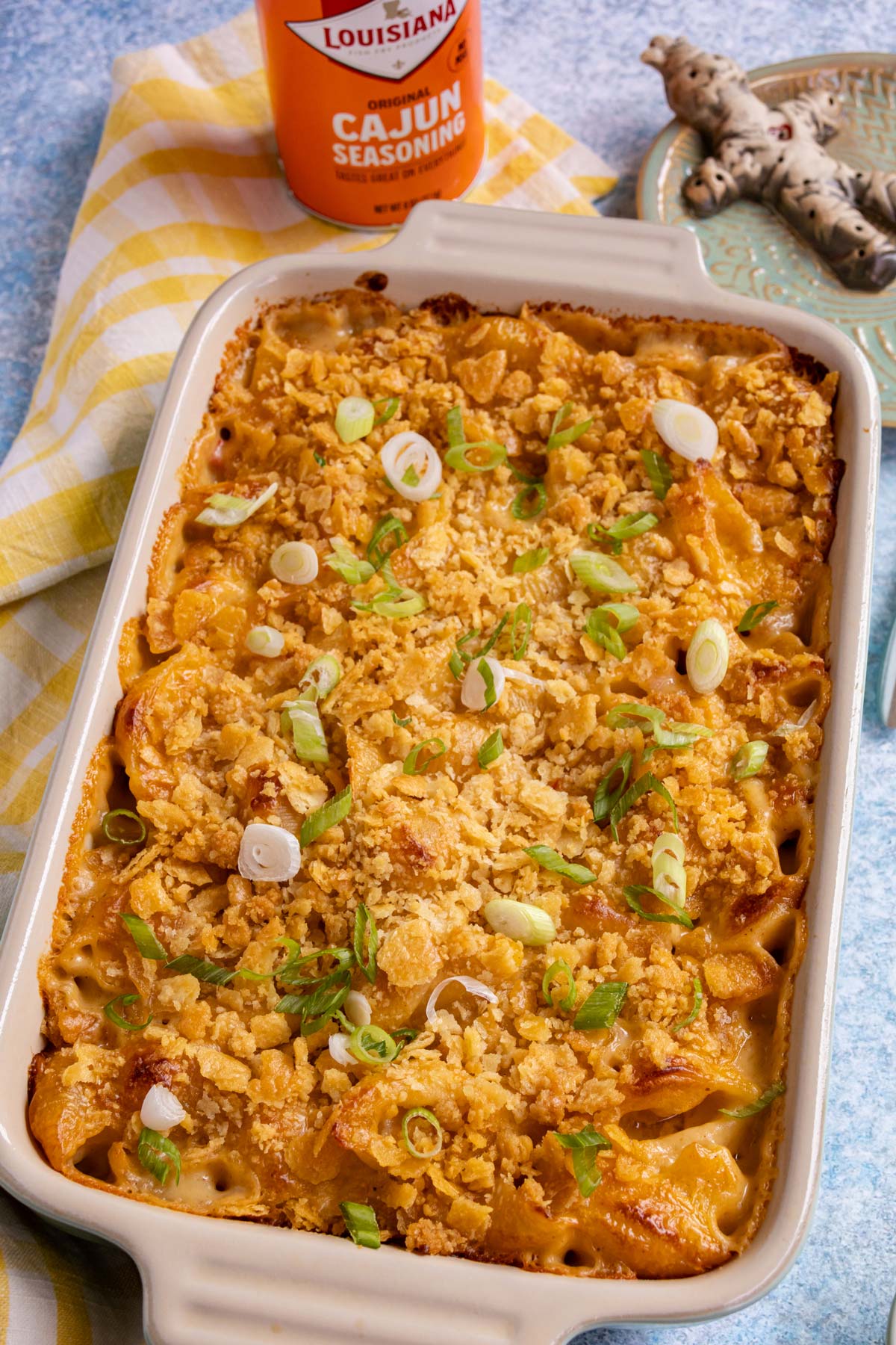 Cajun macaroni and cheese in a rectangular casserole topped with crushed Ritz crackers and sliced scallions.