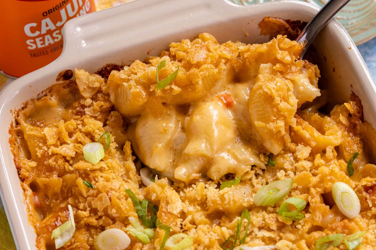A spoon scooping baked Cajun macaroni and cheese out of a casserole dish.