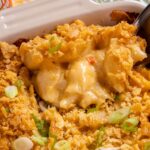 A spoon scooping baked Cajun macaroni and cheese out of a casserole dish.