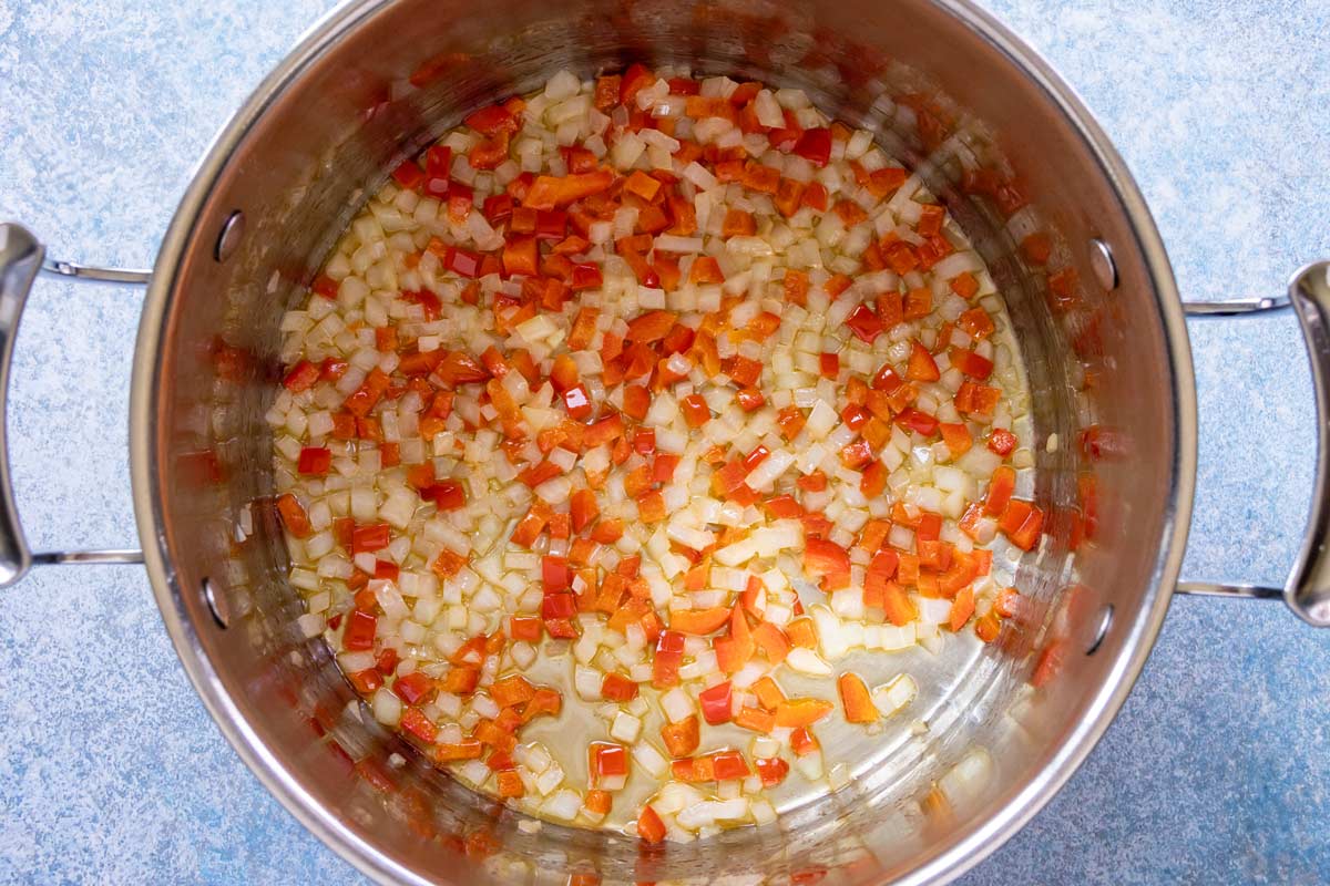 Finely chopped onion and red pepper sauteed in a pot.