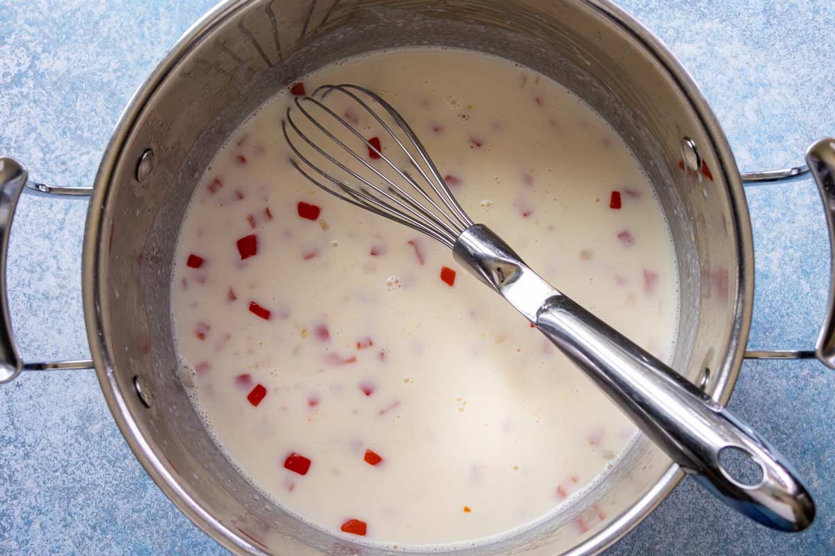 Milk whisked into a pot of roux with onion, pepper, and garlic.
