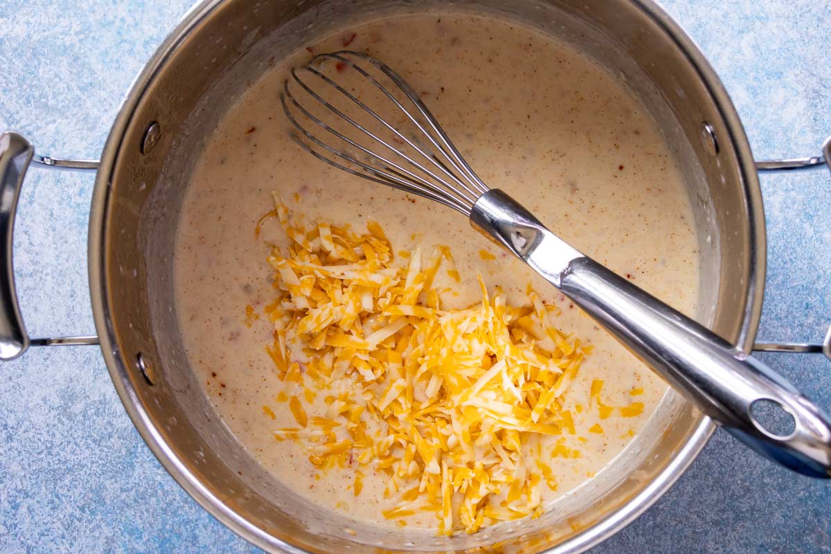 Adding grated cheese to a pot of seasoned bechamel.