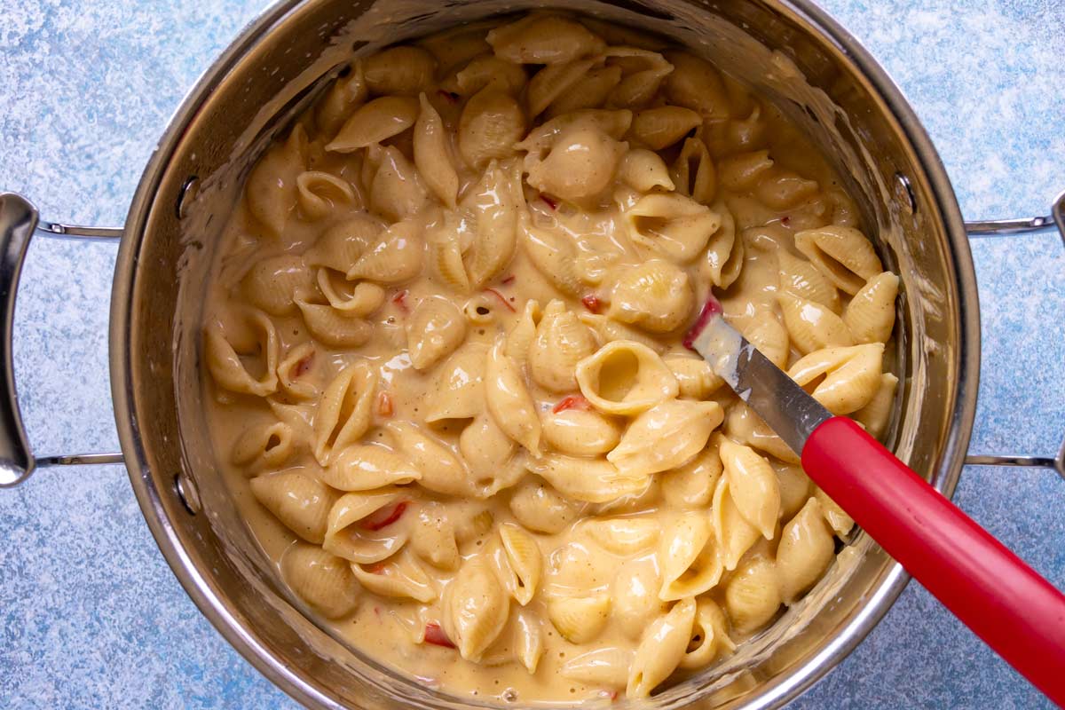 Shells macaroni stirred into a pot of cheese sauce with red peppers and onions.