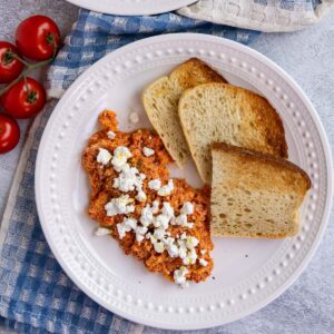 A plate of Greek strapatsada scrambled eggs with tomatoes with toast on the side.