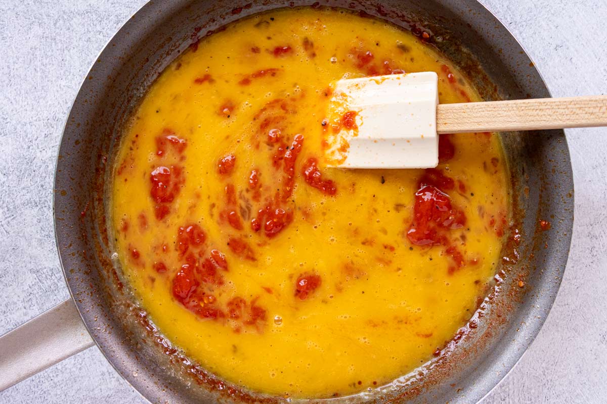 Beaten eggs slowly scrambling into a thick tomato mixture in a nonstick skillet.