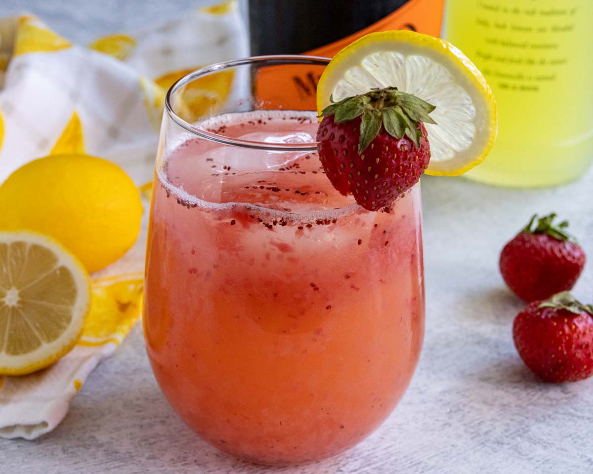 A strawberry limoncello spritz cocktail garnished with a lemon slice and small strawberry on the rim.