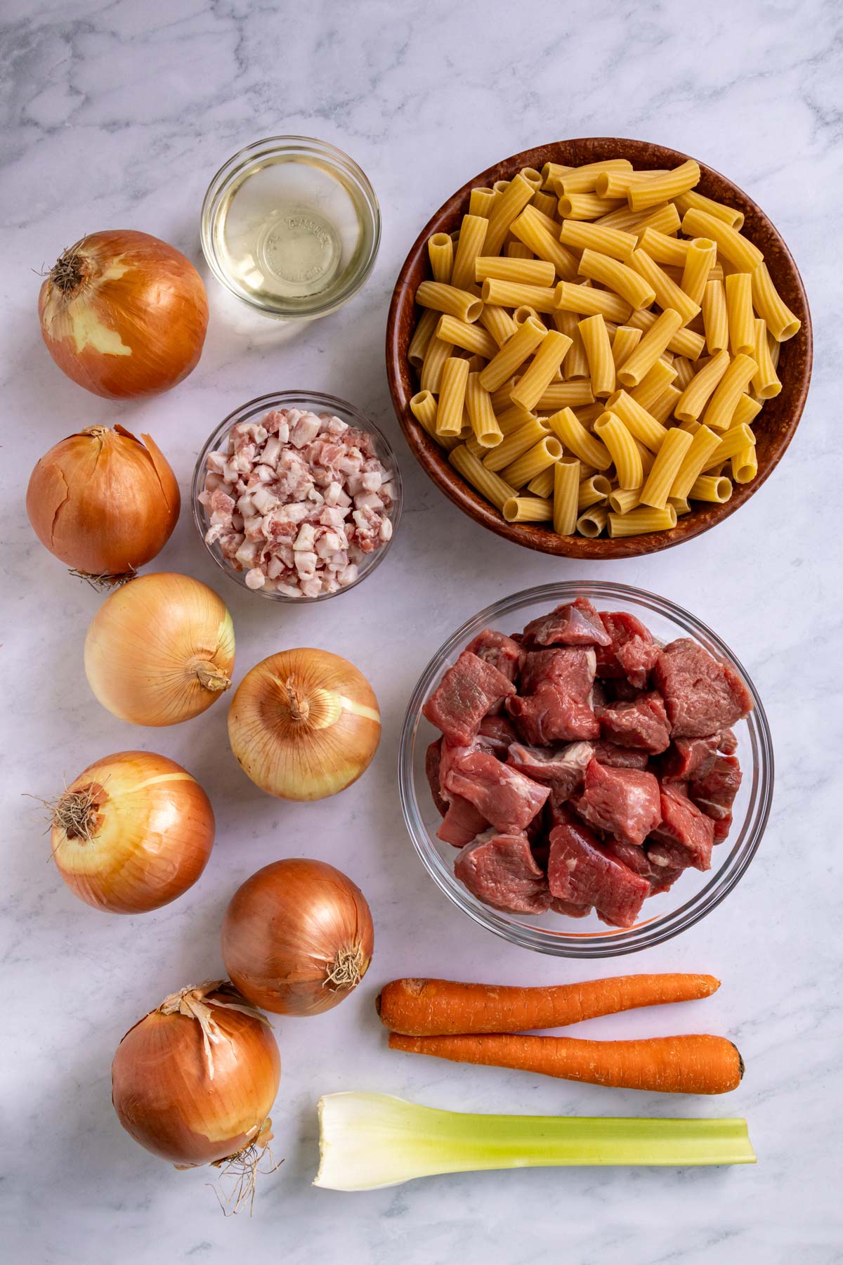 Ingredients for Pasta alla Genovese on a white marble background.