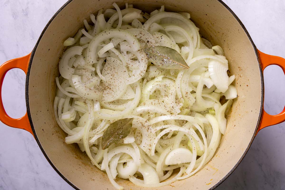Sliced onions and bay leaves added to a Dutch oven.