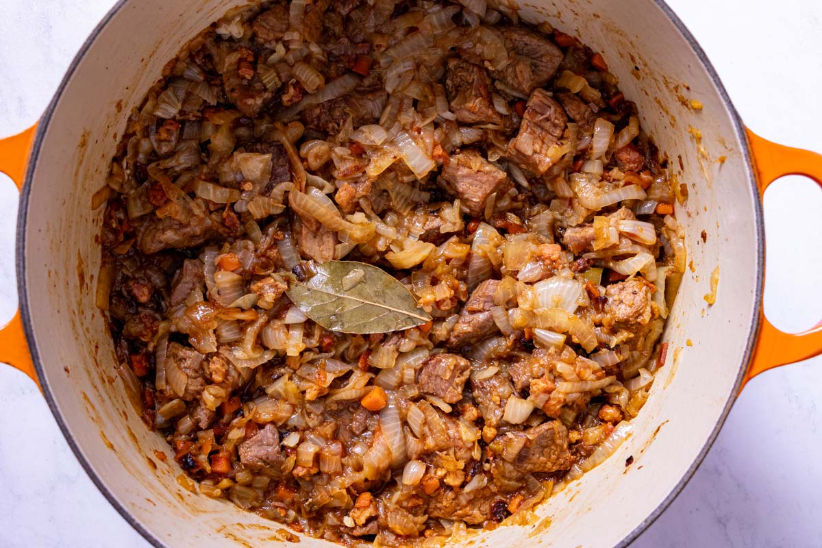 A combination of soft cooked onions and seared beef stewing together in a Dutch oven.