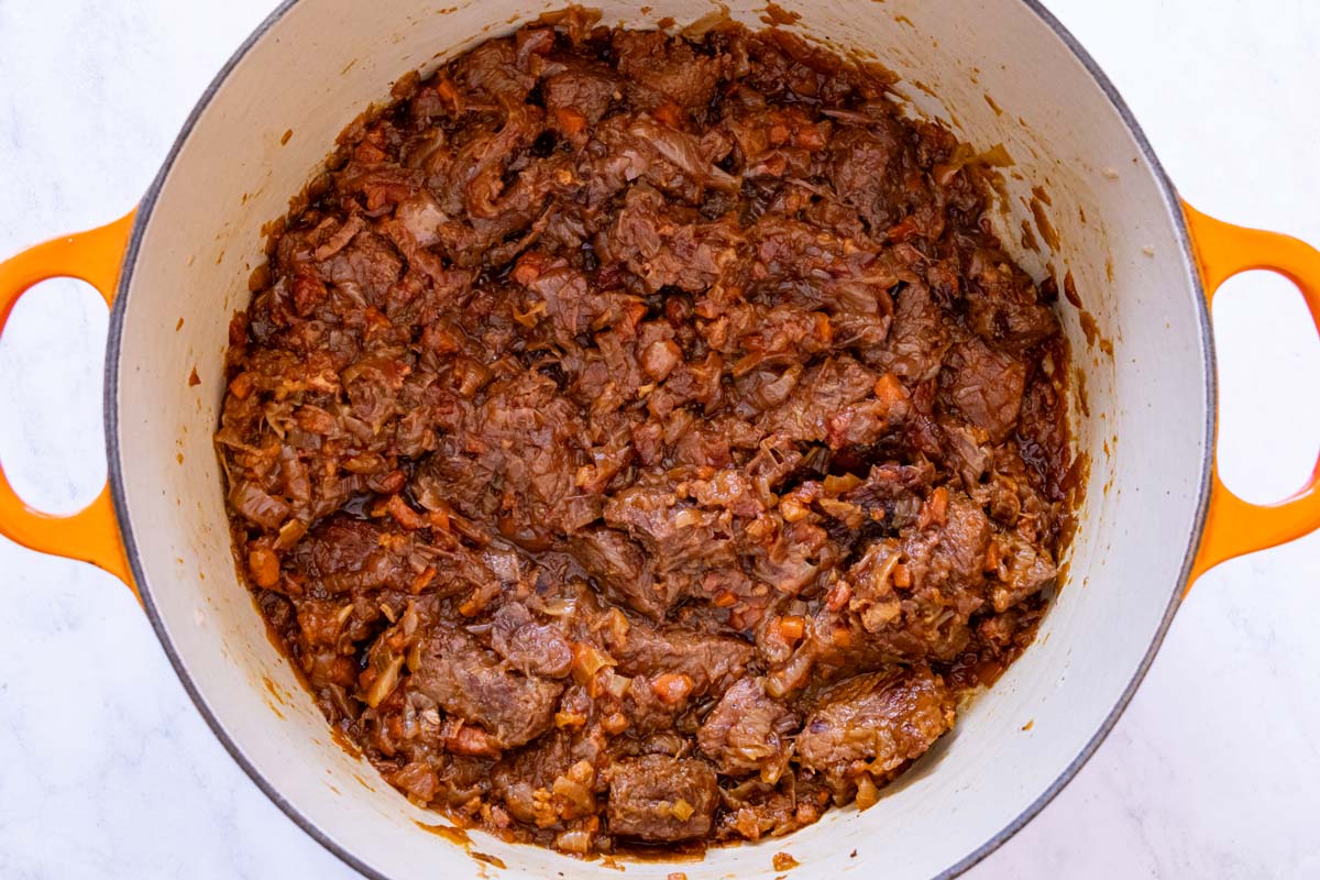 A thick stewed mixture of onions and seared beef in a Dutch oven.