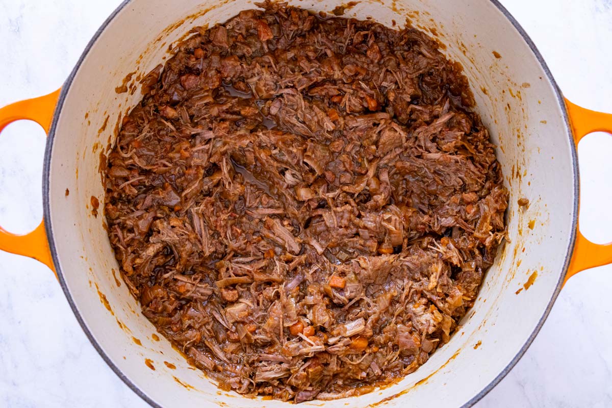 A mixture of shredded stewed beef and slow cooked onions in a Dutch oven.