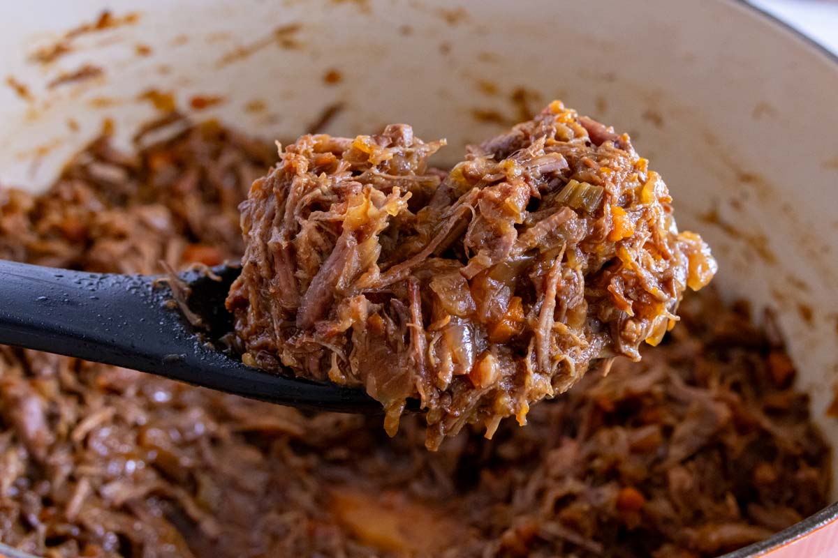 A spoon lifting some sugo alla genovese or Genovese sauce out of a pot.