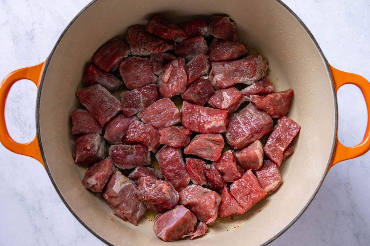 Cubes of seasoned beef chuck added to a Dutch oven.