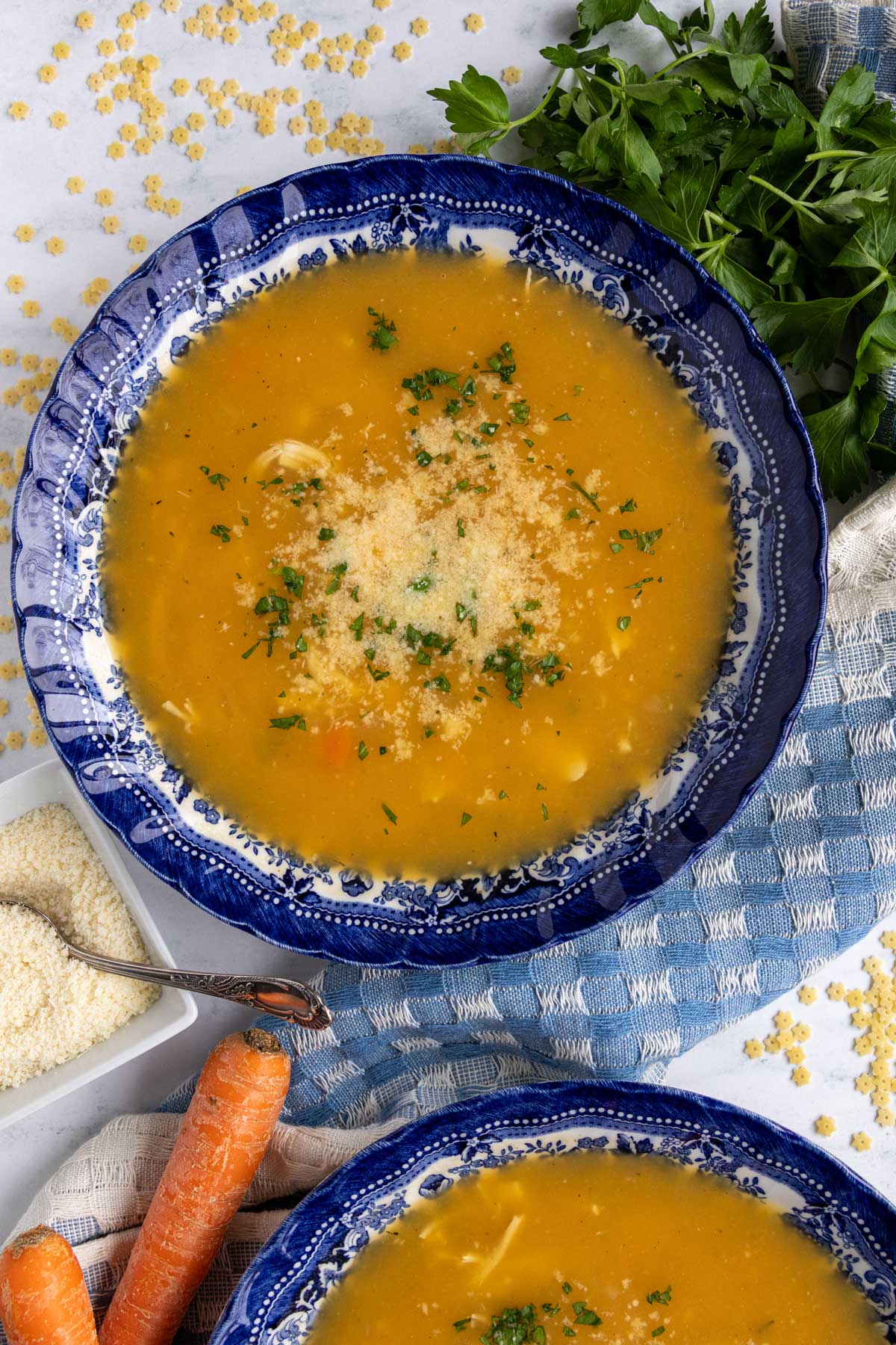 A bowl of Italian chicken pastina soup garnished with chopped parsley and grated parmesan cheese.