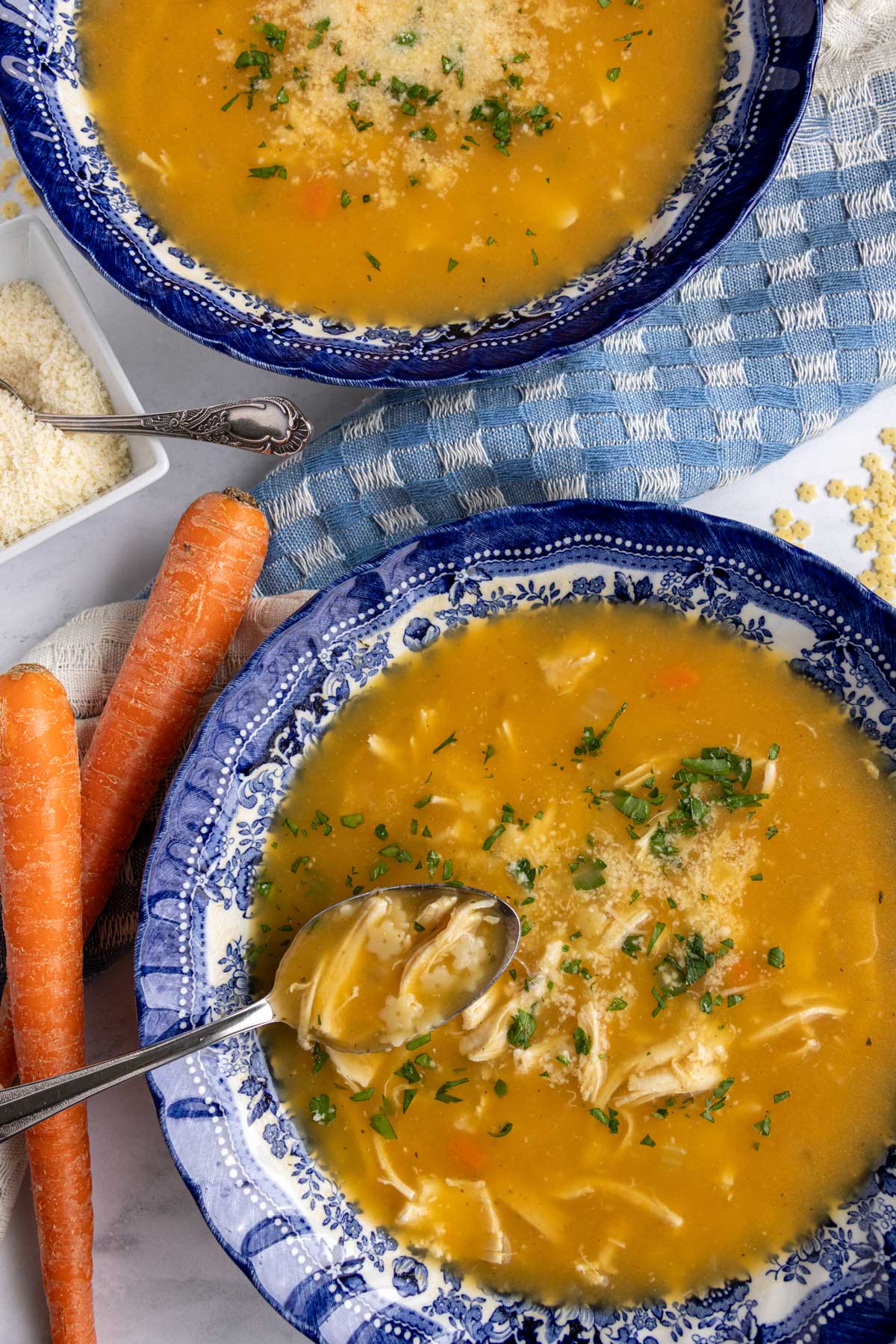 A spoon scooping some chicken pastina soup out of a blue and white shallow bowl.