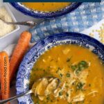 A spoon scooping some chicken pastina soup out of a shallow white and blue bowl.