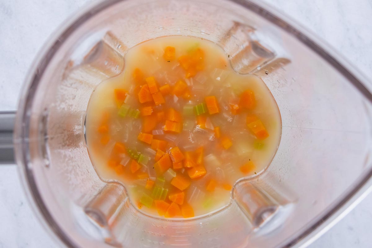 Chopped cooked vegetables and some broth added to the jar of a blender.