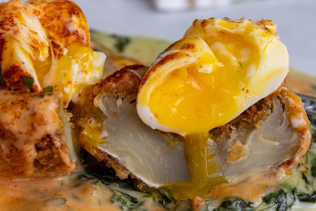 A cross-section of Eggs Sardou showing off the interior of the breaded fried artichoke bottom and the runny poached egg.