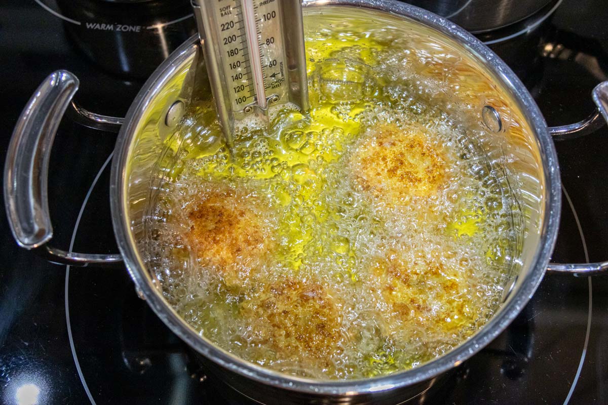 Breaded artichoke bottoms deep frying in a medium pot.