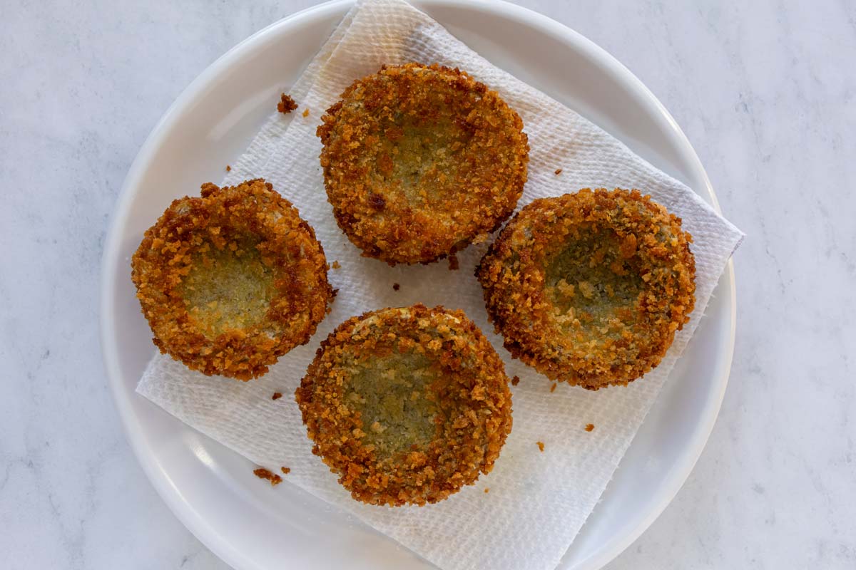 Deep-fried panko-breaded artichoke bottoms draining on a paper towel-lined plate.