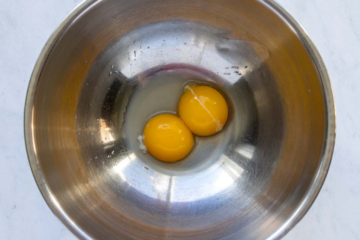 Two egg yolks, lemon juice and white vinegar in a metal bowl.