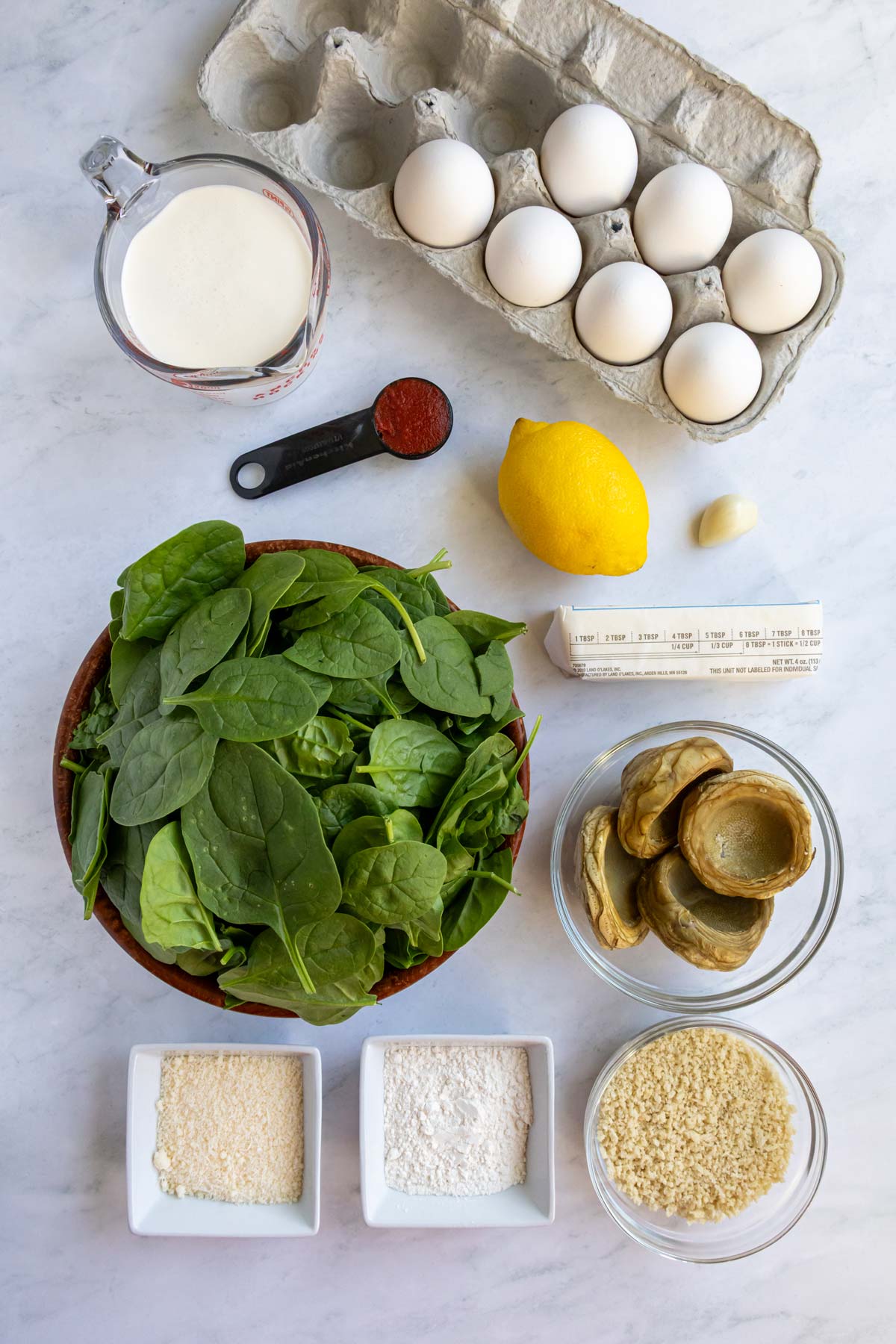 Ingredients for Eggs Sardou on a white marble background.