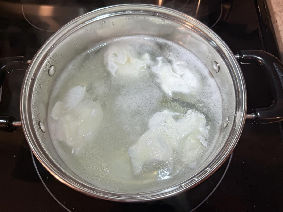 Four eggs poaching in a wide shallow pot.