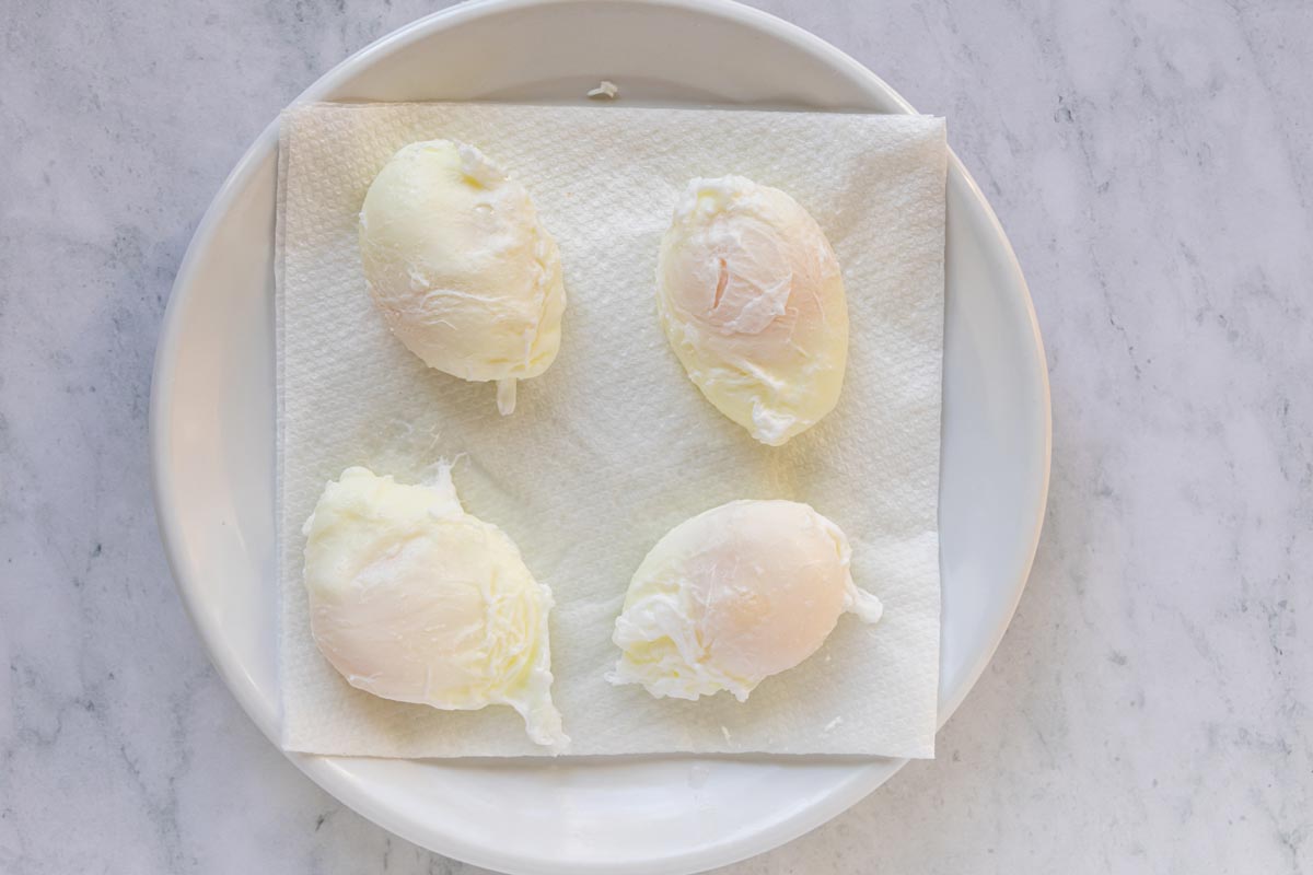 Four poached eggs draining on a napkin-lined white plate.