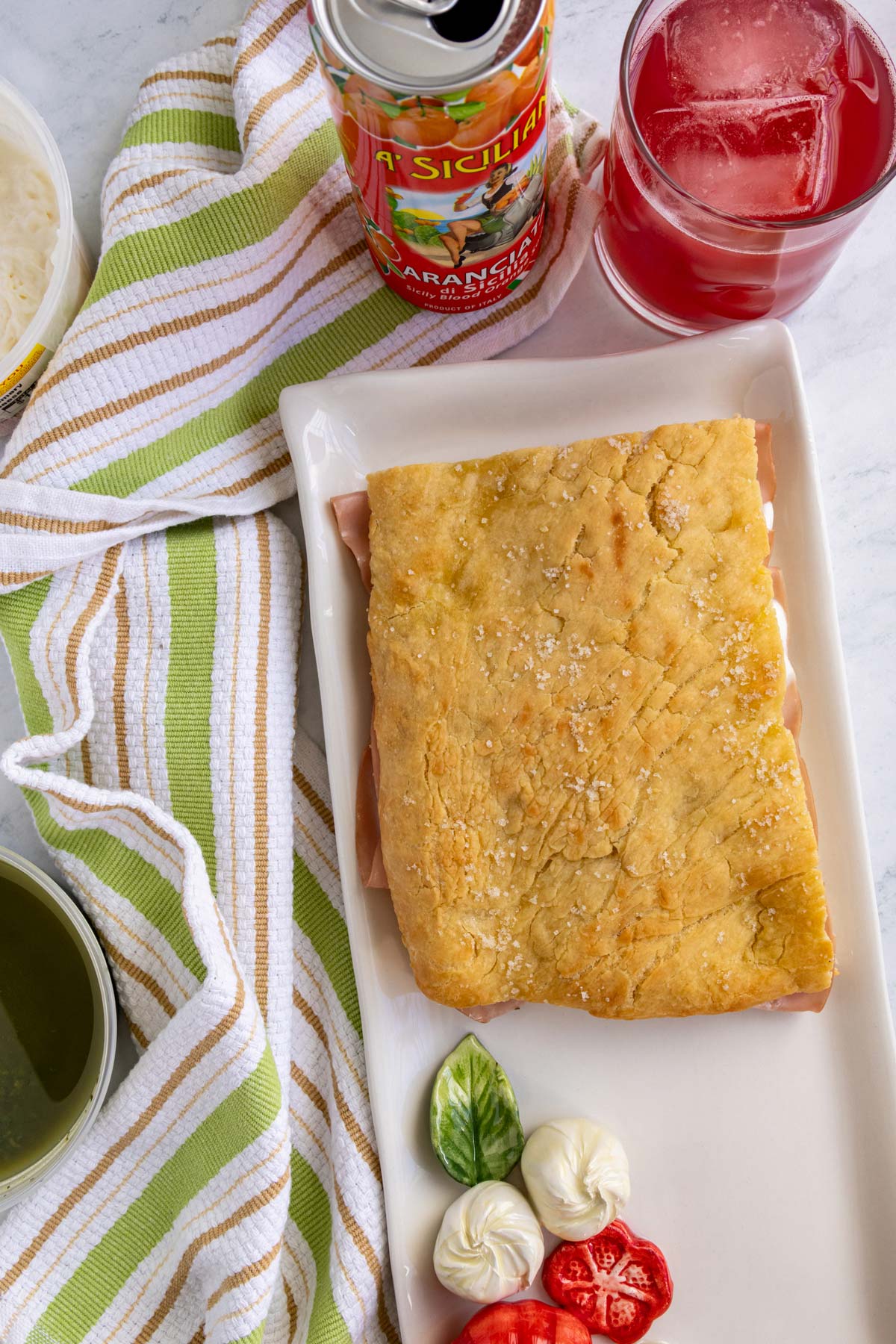 A crispy mortadella sandwich on a Caprese salad-inspired white platter.