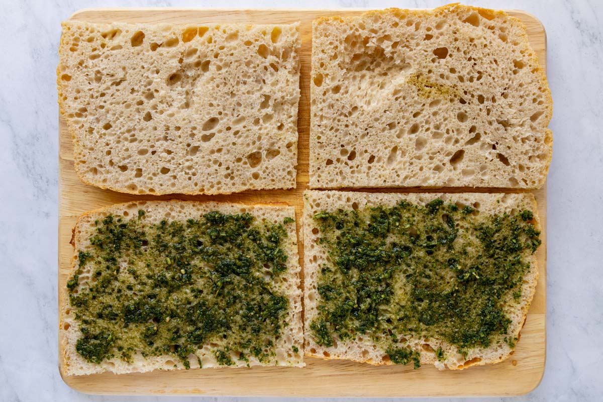 Two pieces of pizza bianca cut open and spread with pesto on the bottom.