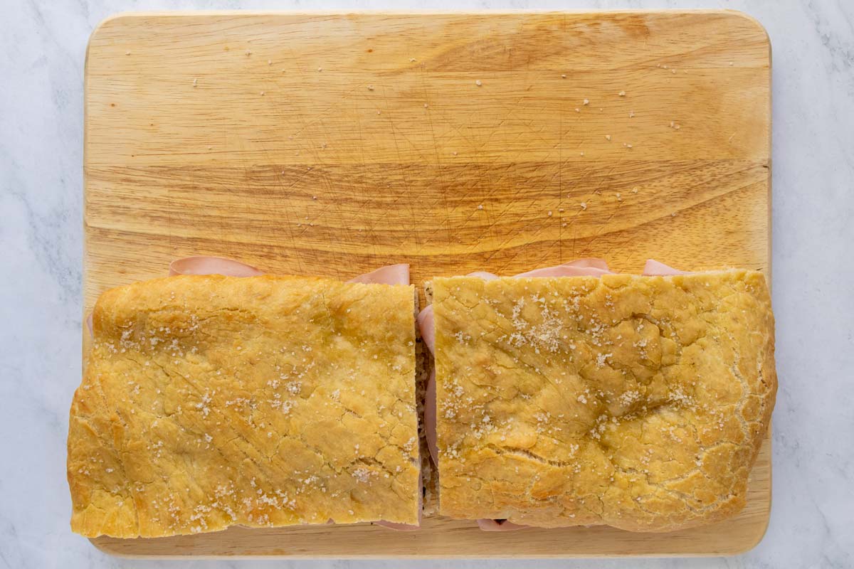 Two mortadella sandwiches on a wooden cutting board.