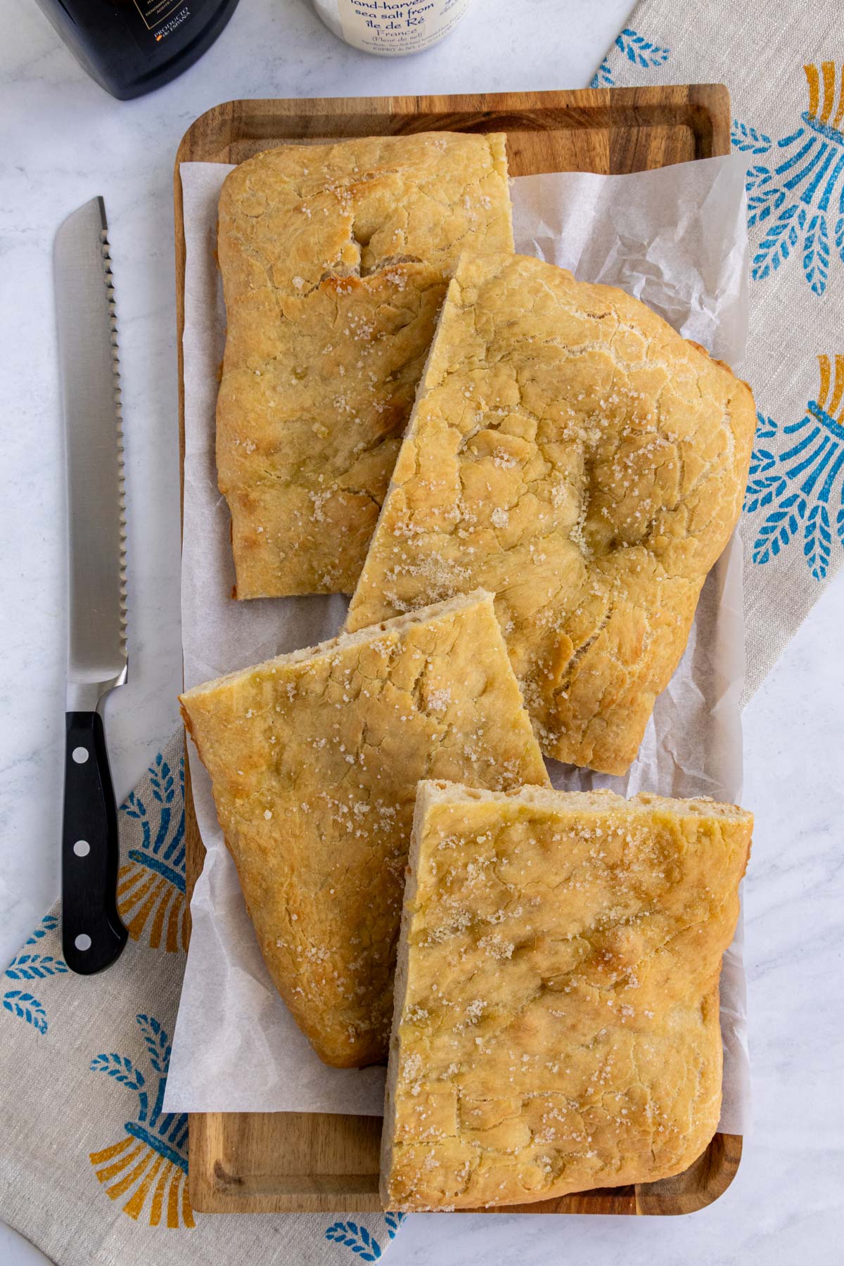 Four rectangular pieces of pizza bianca on a wooden platter with a serrated knife to the left.
