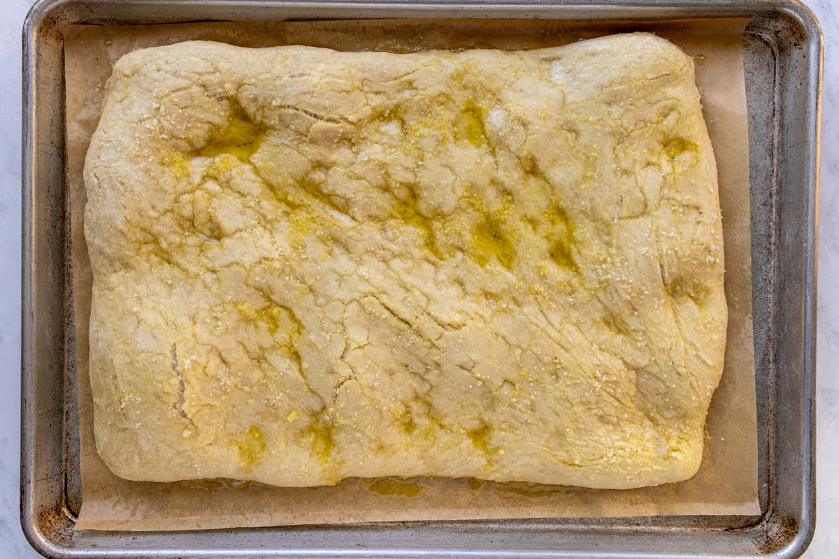 A partially baked pizza bianca on a parchment paper-lined baking sheet.