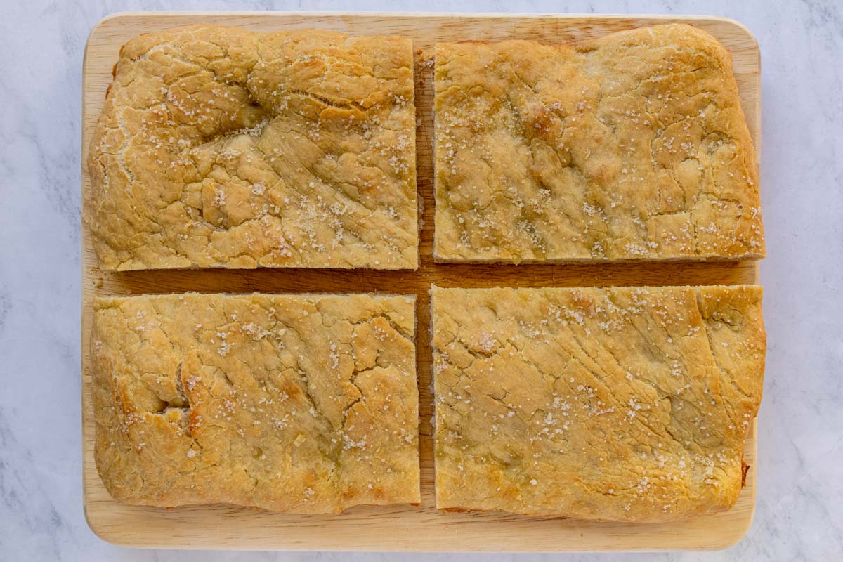 A rectangular pizza bianca cut into four rectangular pieces on a wooden board.