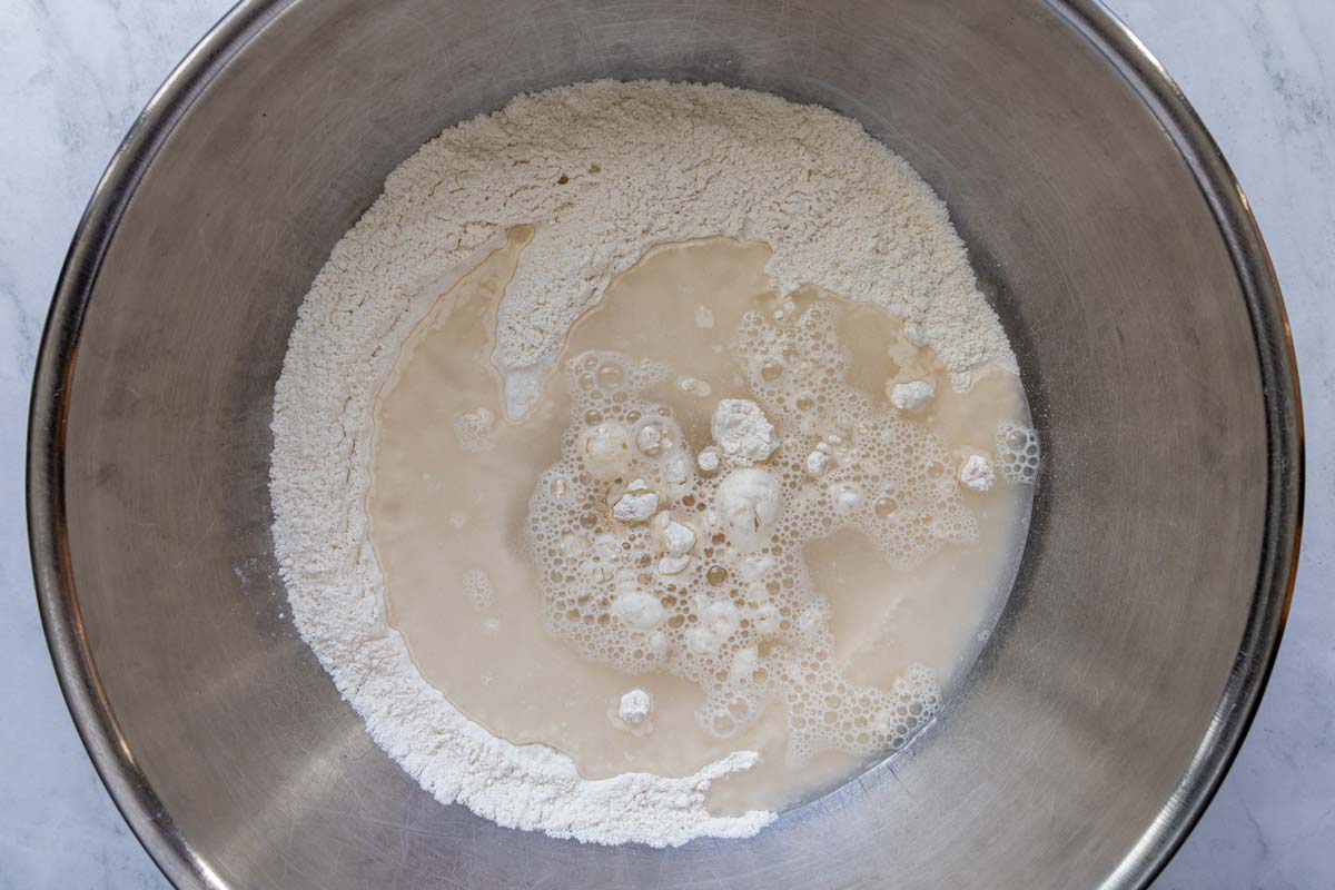 Water added to a mixing bowl of flour, salt, and yeast.