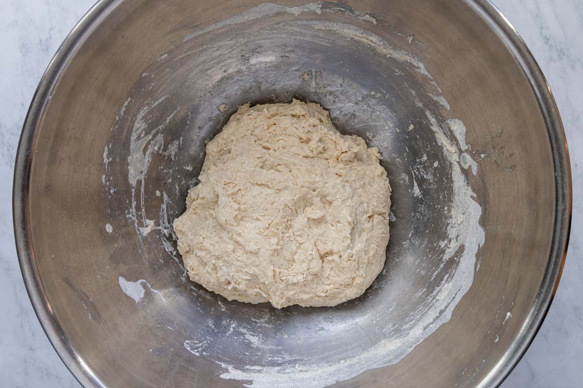 A soft sticky dough in a metal mixing bowl before rising.