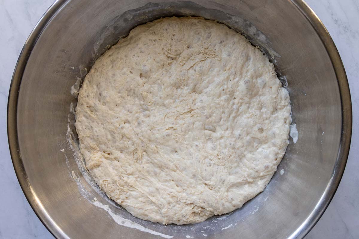 A soft sticky dough in a metal mixing bowl after rising.