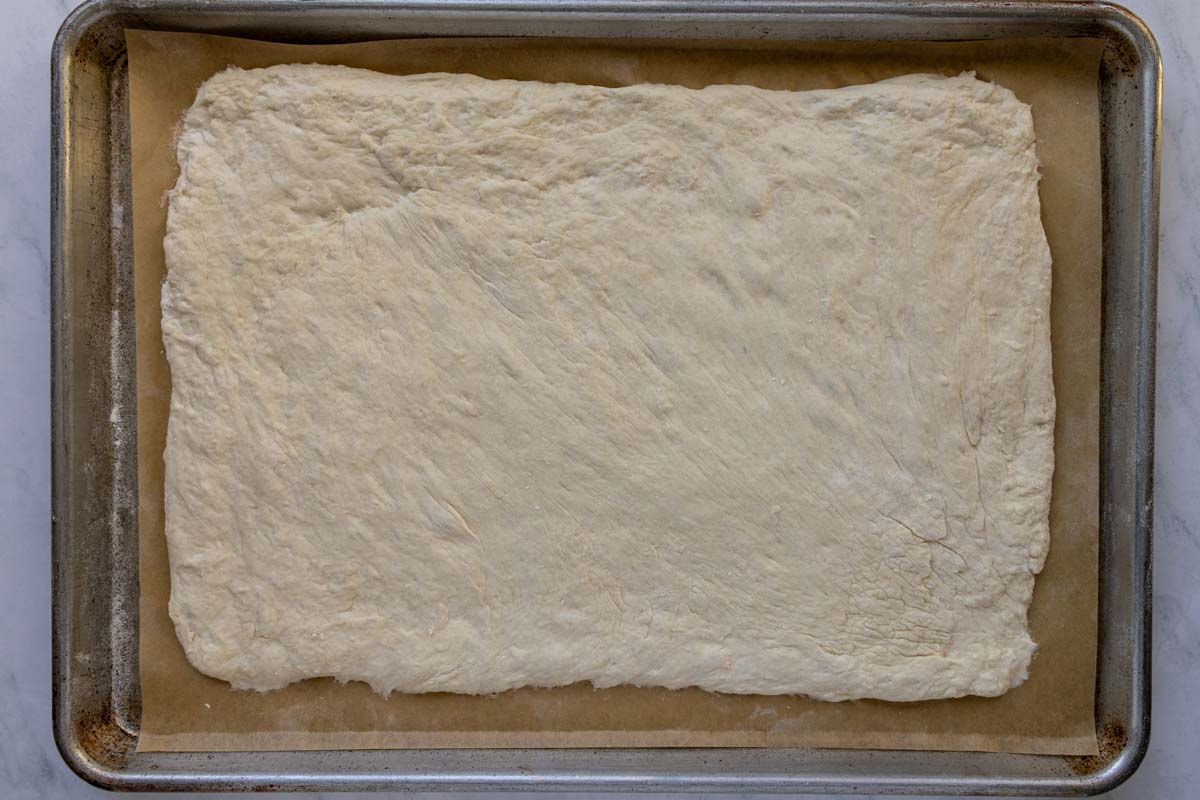 A soft sticky dough stretched into a rectangle on a flour-dusted parchment paper-lined baking sheet.