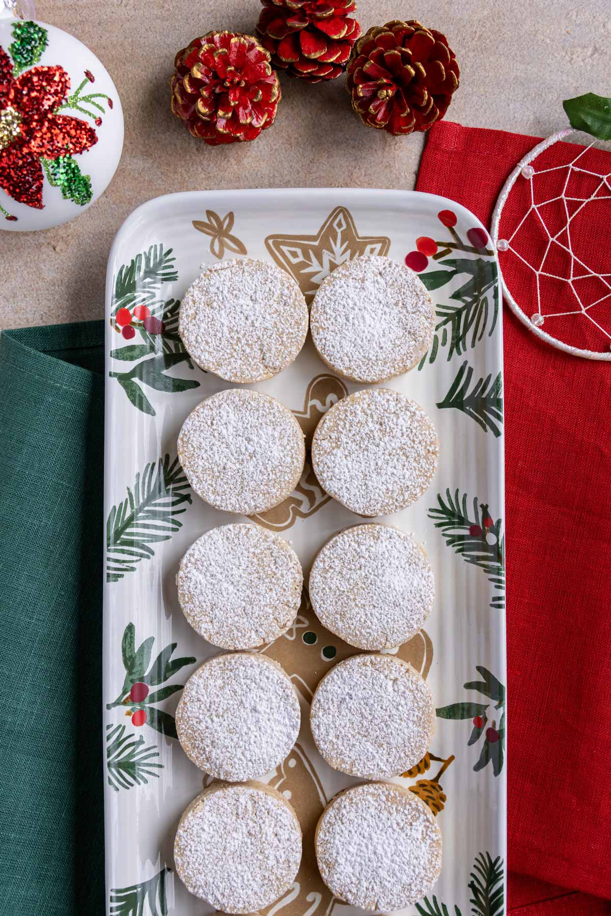 Polvorones shortbread cookies on a holiday platter next to ornaments and red holiday-themed pinecones.