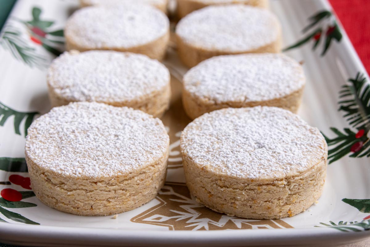 Round Spanish polvorones cookies topped with powdered sugar on a Christmas-themed platter.