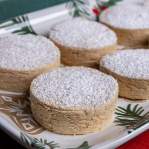 Round Spanish polvorones cookies topped with powdered sugar on a Christmas-themed platter.
