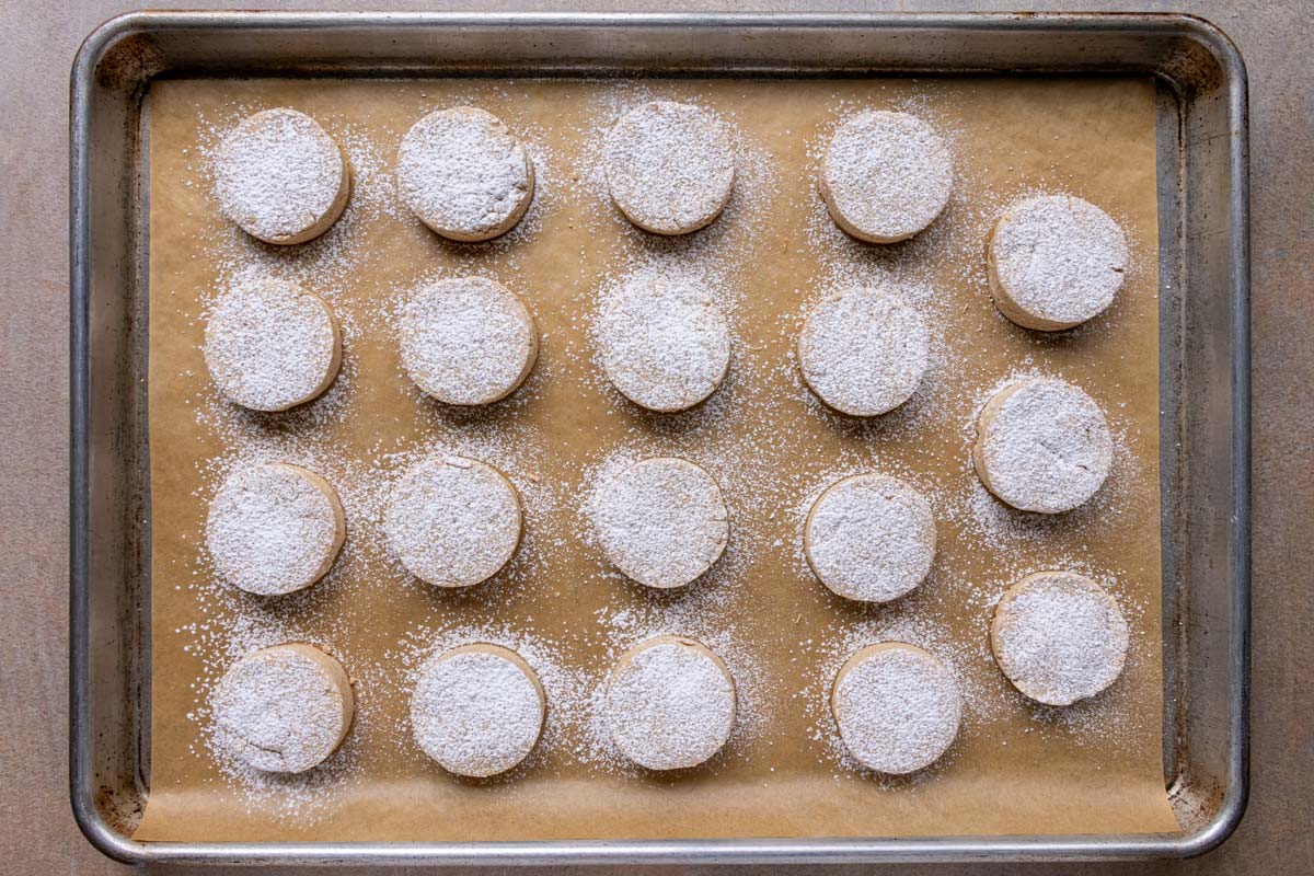 Round Spanish polvorones cookies dusted with powdered sugar on a baking sheet.