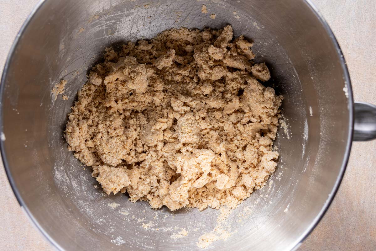 A more cohesive but still crumbly dough mixture in a mixing bowl.