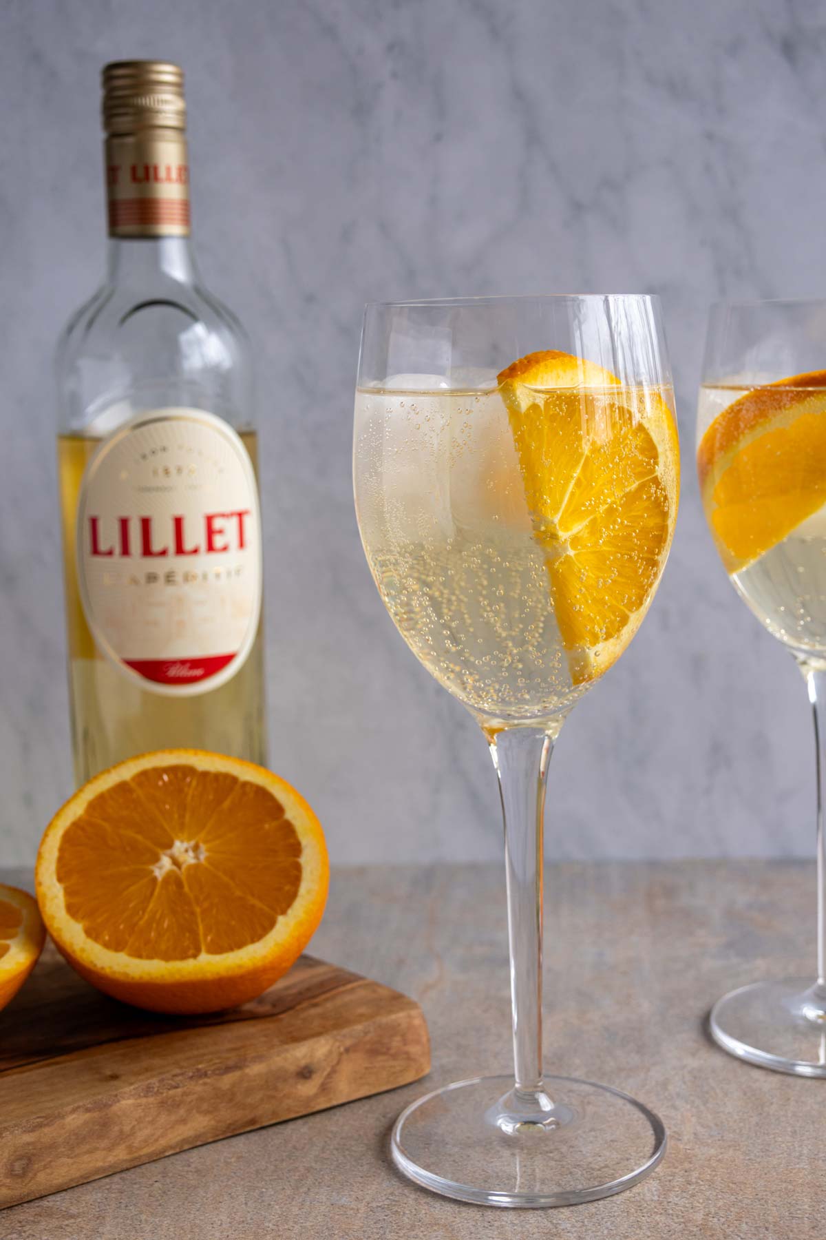 A glass of Lillet Spritz next to small cutting board with a halved orange on it.